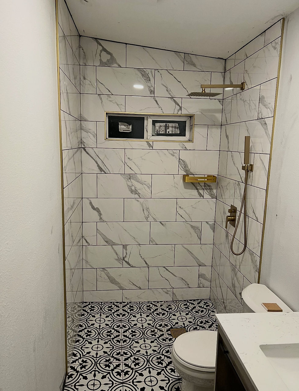 Modern walk-in shower with marble tile and gold fixtures.