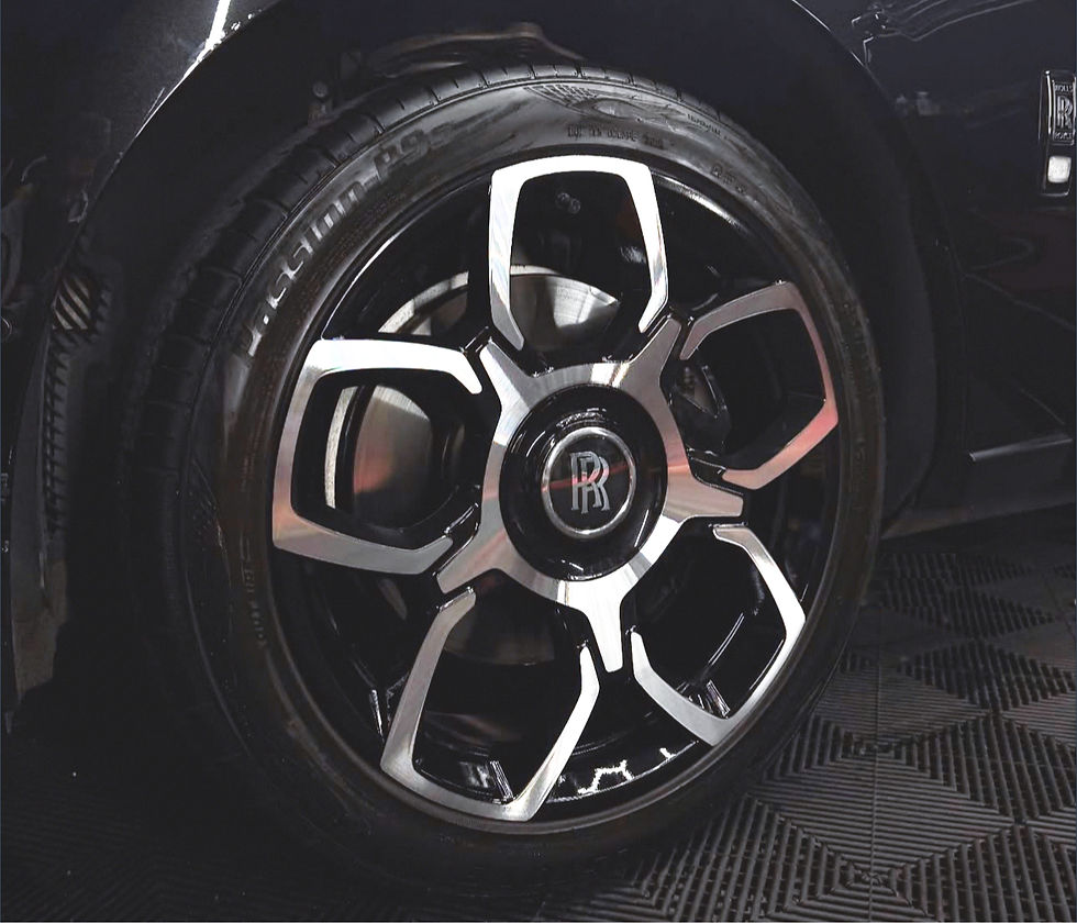 Close-up of a Rolls-Royce wheel with black-and-silver rim, RR logo center cap, on a dark patterned floor.