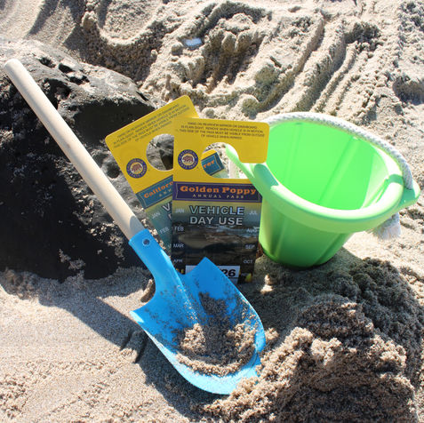 Two parking passes posed in beach sand next to a bucket and shovel