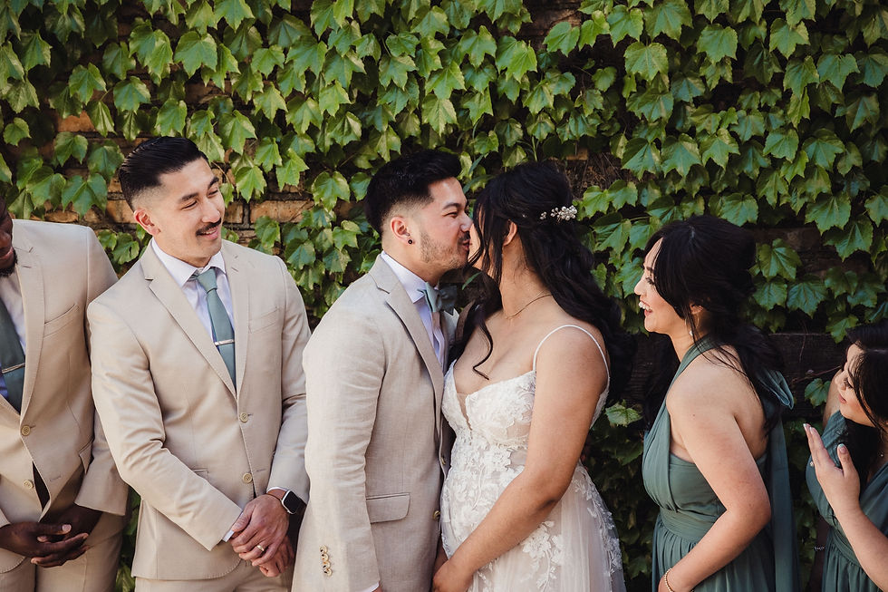 Bride and groom kissing while wedding party looks on