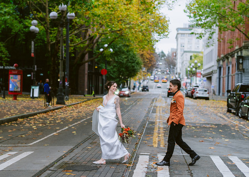 wedding couple holding hands looking at each other walking down sidewalk with trees and fall leaves