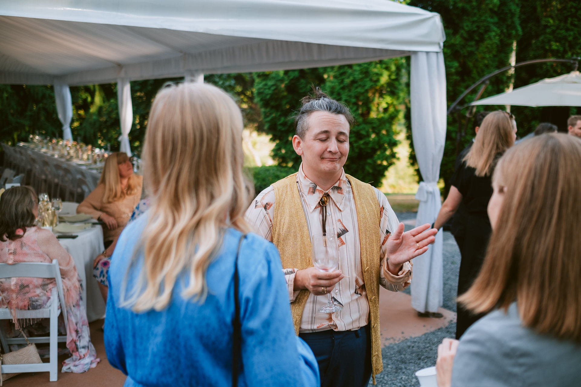 Wedding guest in bolo tie and vest talking with friends on a sunny day