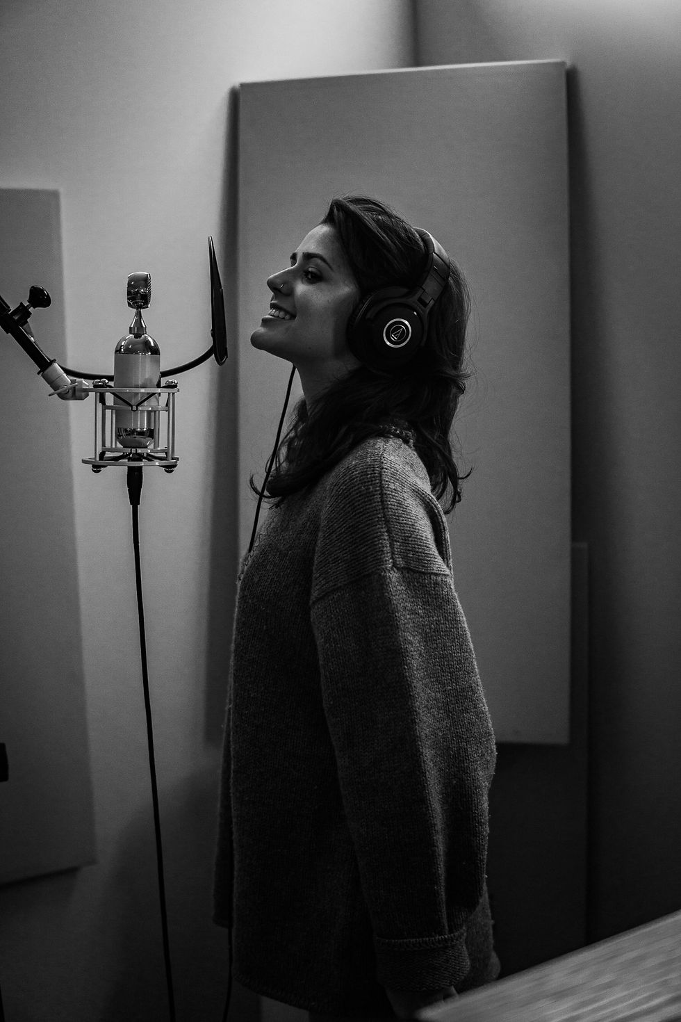 Country music artist smiles as she sings into a microphone while in studio.