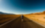 A man walking along the road towards the horizon.