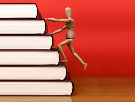 A wooden figure climbing a stack of books arranged like a staircase, signifying kaizen as an approach to continuous improvement