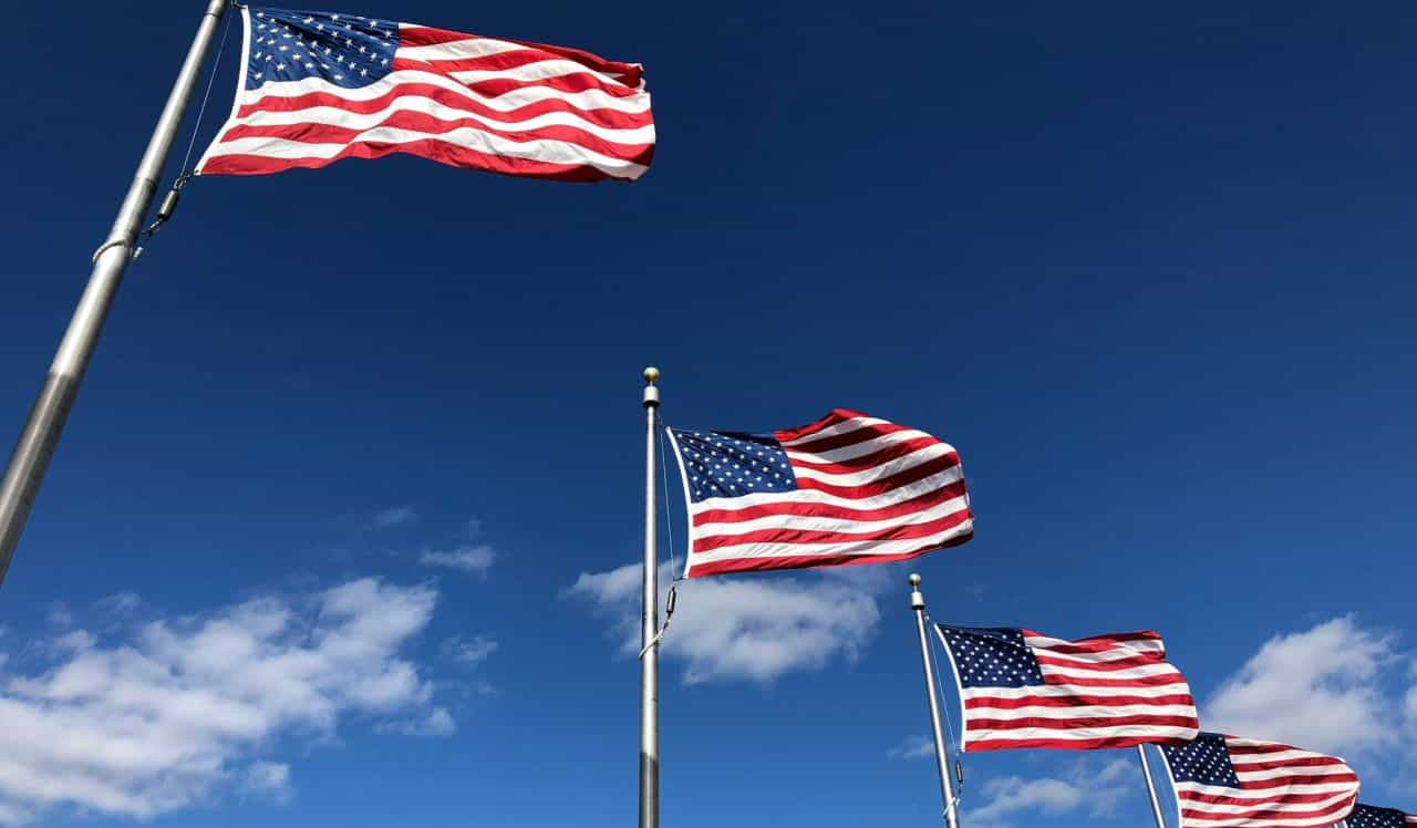 Several American flags wave on tall poles against a bright blue sky with a few clouds.