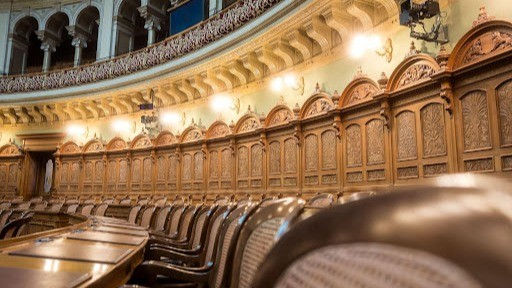 Interior of an ornate government council chamber with wood-paneled seating.