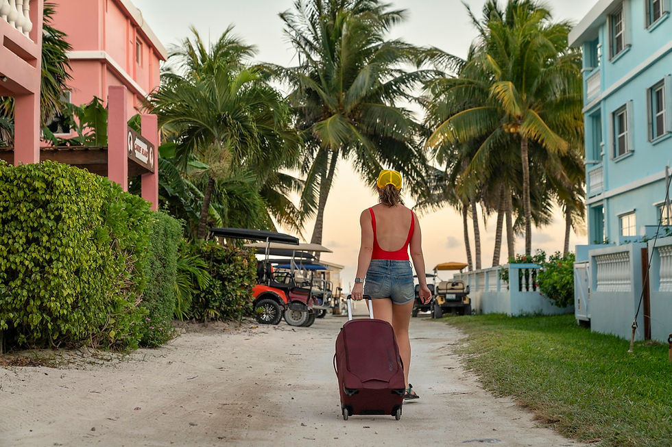 Woman rolling Eagle Creek burgundy luggage down a sandy palm-lined path on a tropical island.
