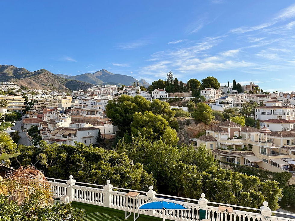 Scenic view of Nerja with mountains, sun, houses, and clear skies.