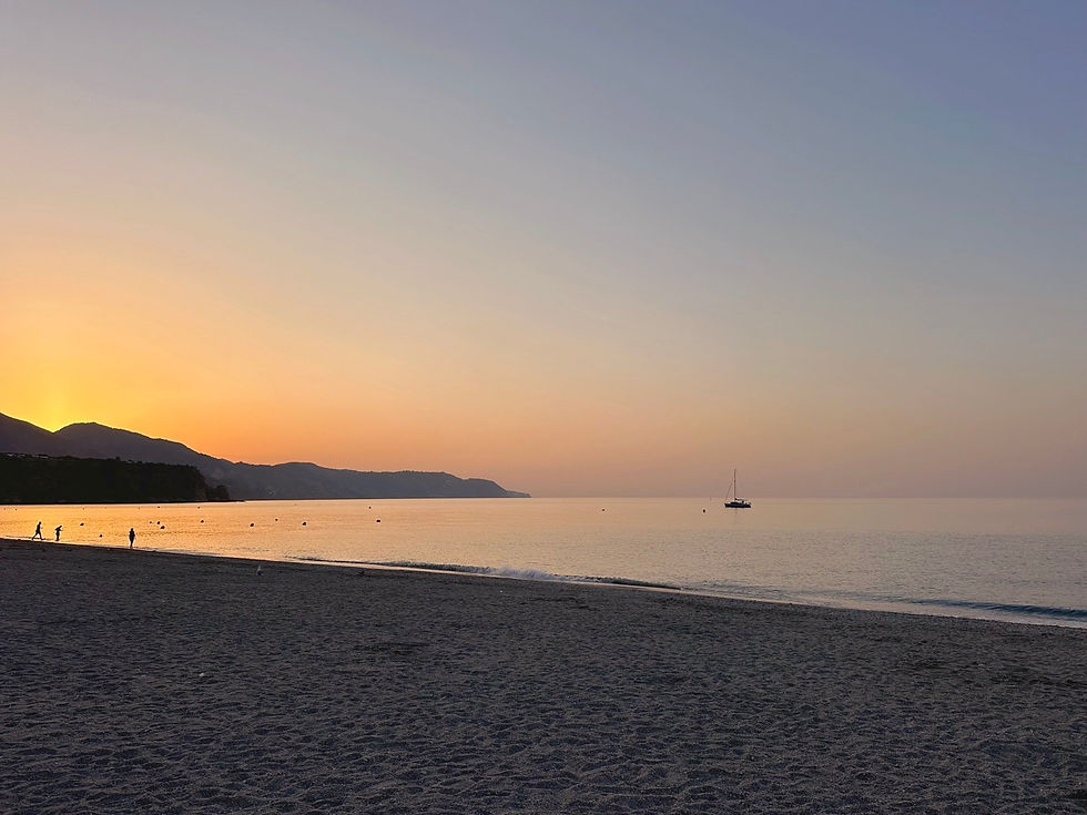 Amanecer dorado sobre Playa Burriana en Nerja, iluminando la arena y el mar con luz cálida