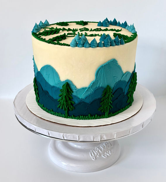 Cake with fading blue ombre mountains and green trees.
