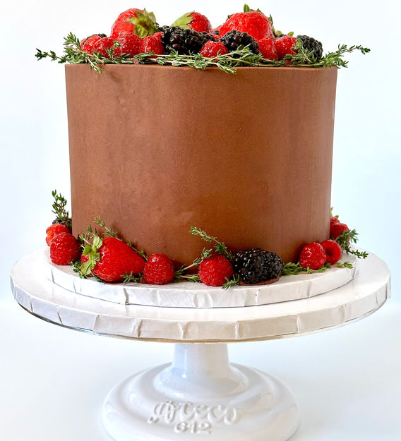 Chocolate cake with berries and herb decoration on top and around bottom.