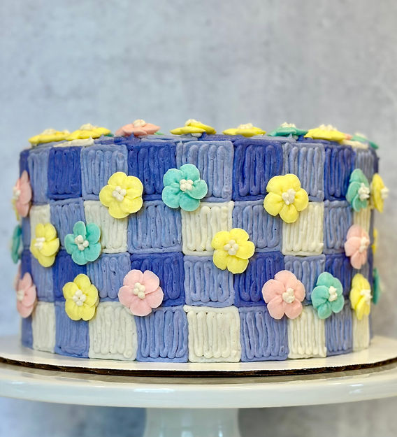 Purple and white gingham cake with piped buttercream pink, yellow, and blue buttercream flowers.