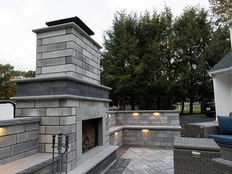 Outdoor fireplace with a stone seating wall with built-in lighting on a paver patio.