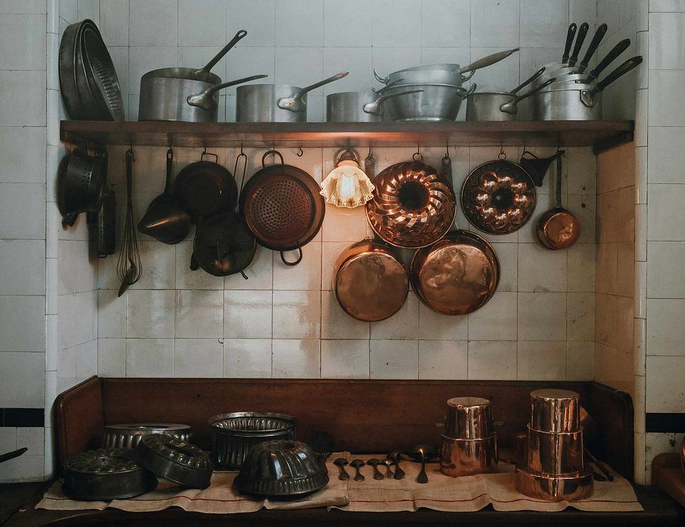 Dense wall-mounted storage of copper pans and stacked metal molds in a compact kitchen, illustrating standardized circular forms and high object density under limited space.