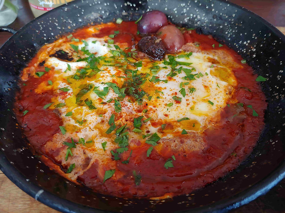 Shakshuka cooking in a pan with reduced tomato sauce and eggs poaching in the sauce.