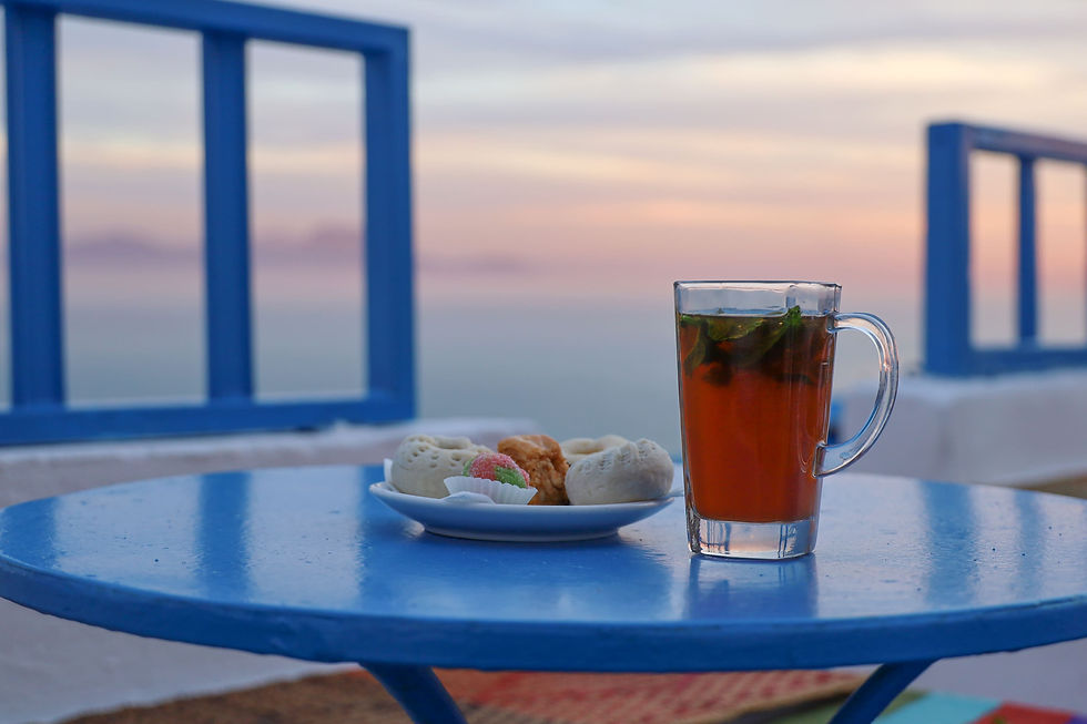 Glass of Tunisian mint tea with pastries on a blue table in Sidi Bou Saïd at sunset — a symbol of Tunisian hospitality and balance.