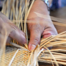 Hands weaving natural fibers into a traditional basket by hand.