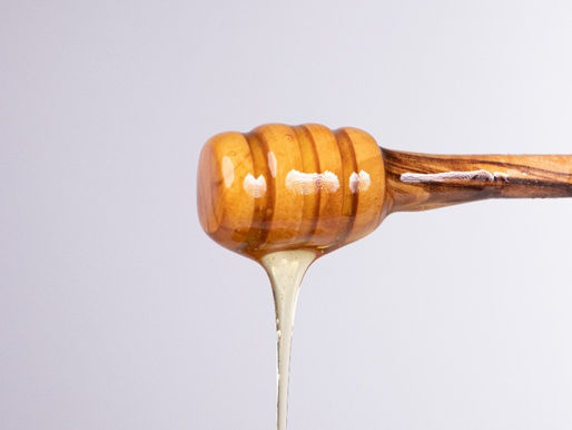 Olive wood honey dipper with raw Tunisian honey slowly dripping against a plain background.