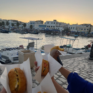 Fricassé sandwich held near a coastal harbor in Tunisia, showing how it is eaten in everyday settings