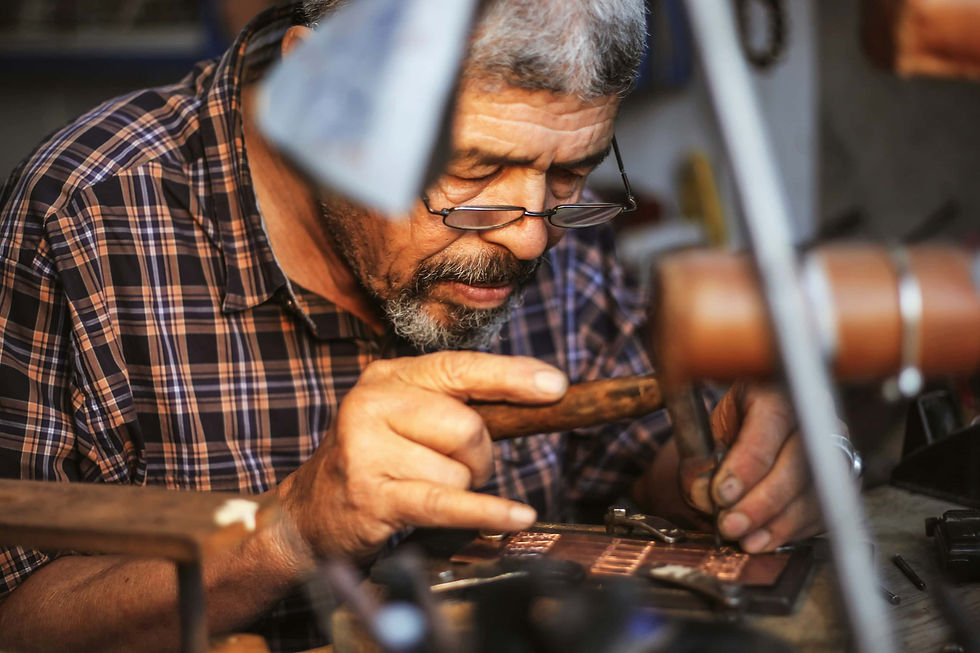 Artisan working with hand tools on a small metal piece in his workshop.