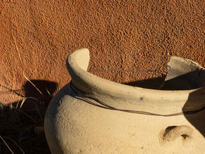 Repaired clay vessel with visible wire reinforcement stabilizing a cracked rim under Mediterranean use conditions.