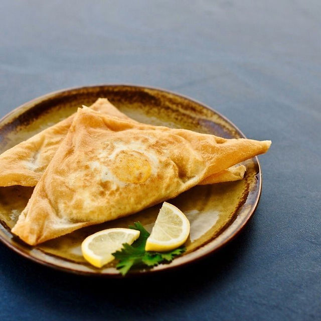 Crispy Tunisian brik pastry on a plate with lemon wedges
