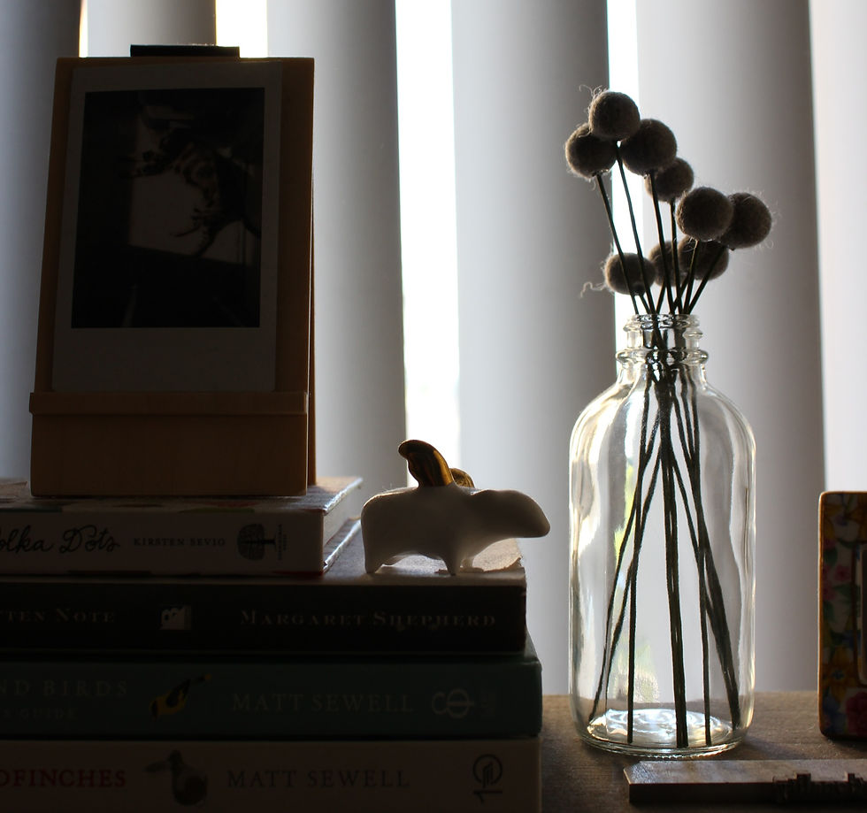 Photo: Kimberly's studio close-up of a stack of books, flying pig ceramic figurine, jar of felt flowers
