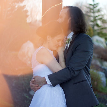 Bride snuggled in close to groom who has arms locked around her waist and is nuzzling her hair in gazebo with greenery behind and a light flare atkinson country club new hampshire wedding photography