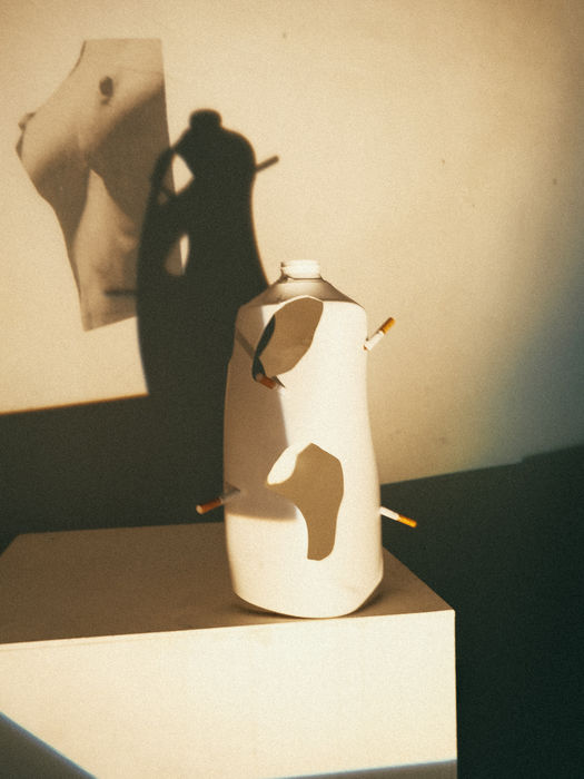 Image of a plastic detergent canister altered with holes and cigarette butts and a projected nude body, evoking themes of addiction and consumer identity. From Things We Held in Silence, Alexander Libotte, 2026.