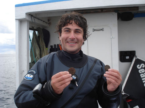 Man on boat, holding coins from shipwreck.