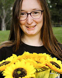 Jessica wearing a black shirt and holding a large bouquet of yellow sunflowers, smiling
