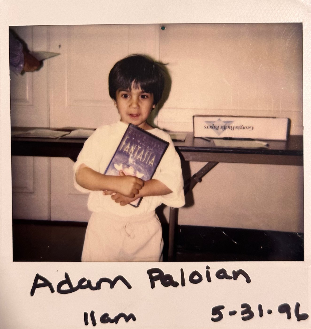 Polaroid of young Adam hugging a Fantasia VHS, labeled Adam Paloian, 5-31-96