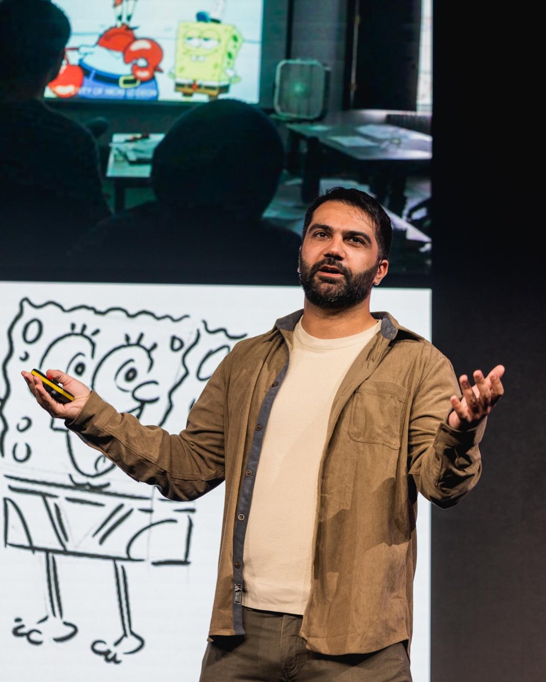 Adam speaking on stage at Playgrounds in Eindhoven, in front of a slide of a SpongeBob drawing