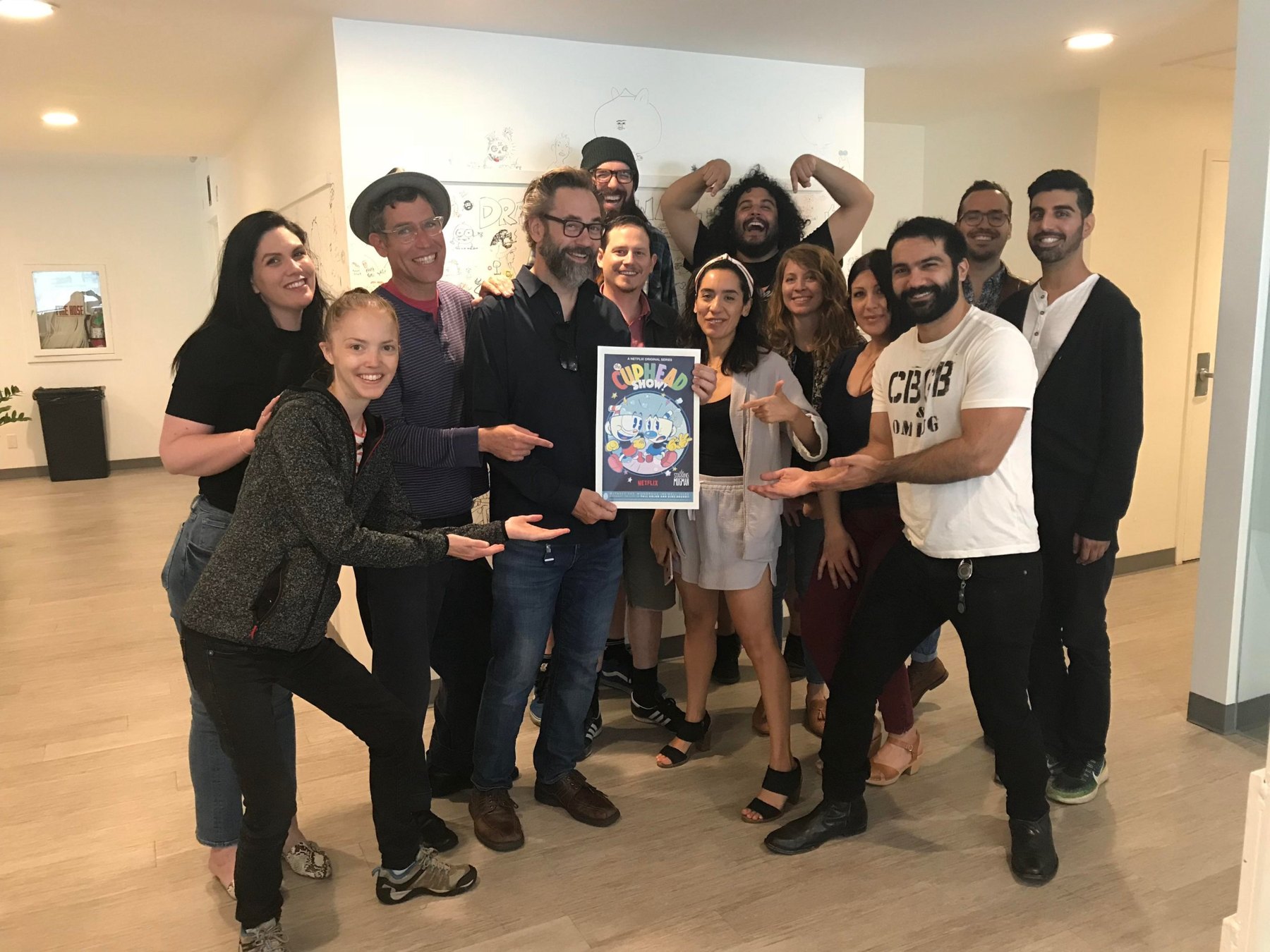 The crew gathered around the first Cuphead Show! poster, pointing at it