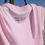 Thumbnail: Close-up of pink Parri Jamaica tee with “Out of Many, One People” text on the back neckline.