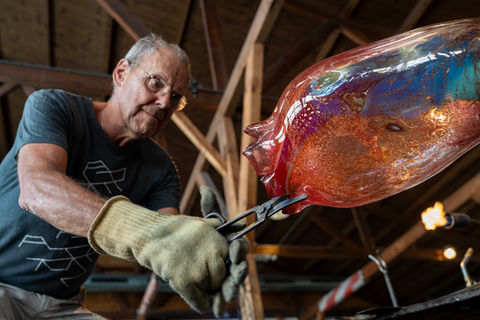Portret van glaskunstenaar Fons Uytdehaag aan het werk met heet glas in zijn atelier