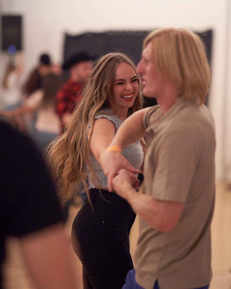 A young adult couple makes each other laugh while they dance.