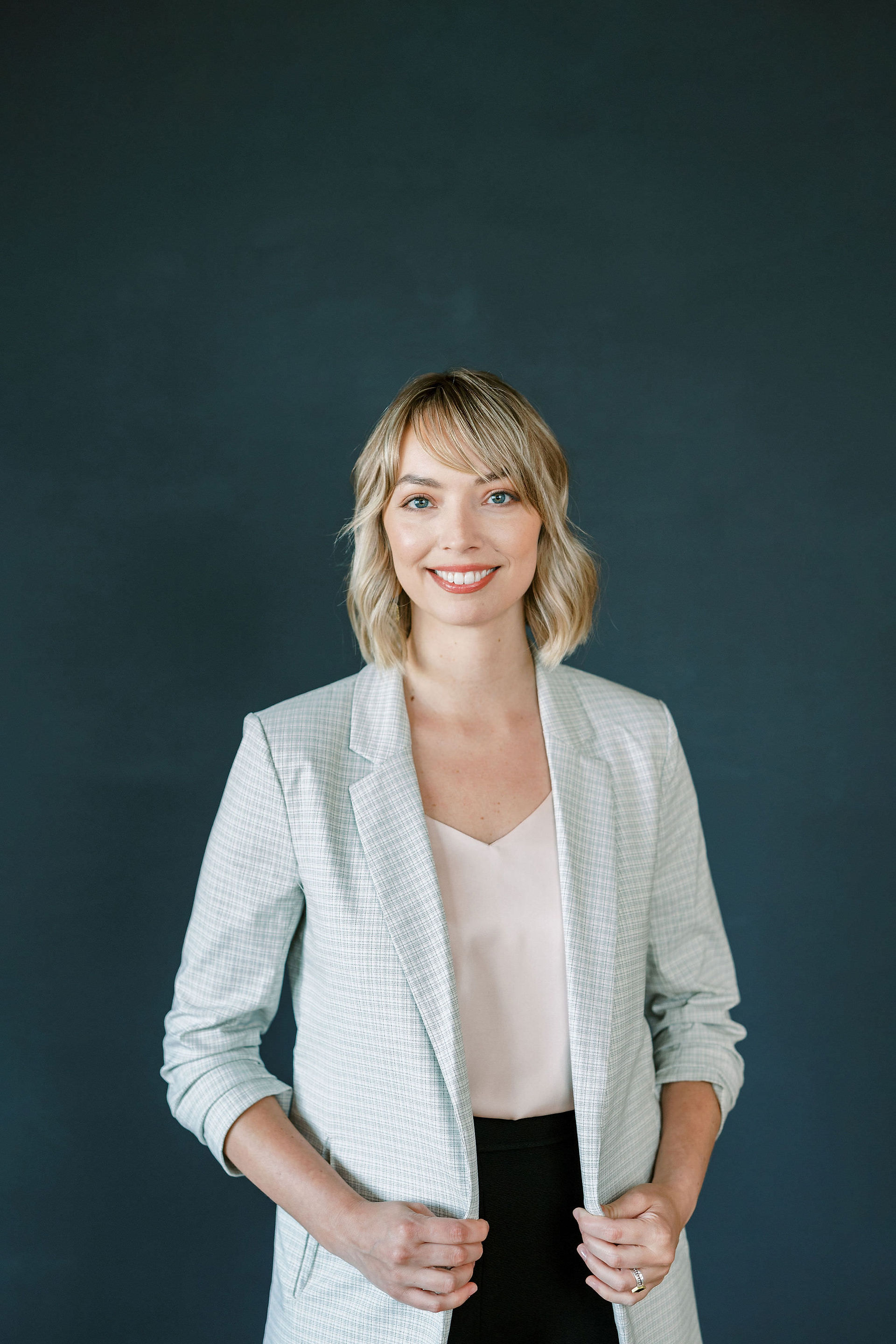 Woman standing holding blazer jacket in front of a gray background. 