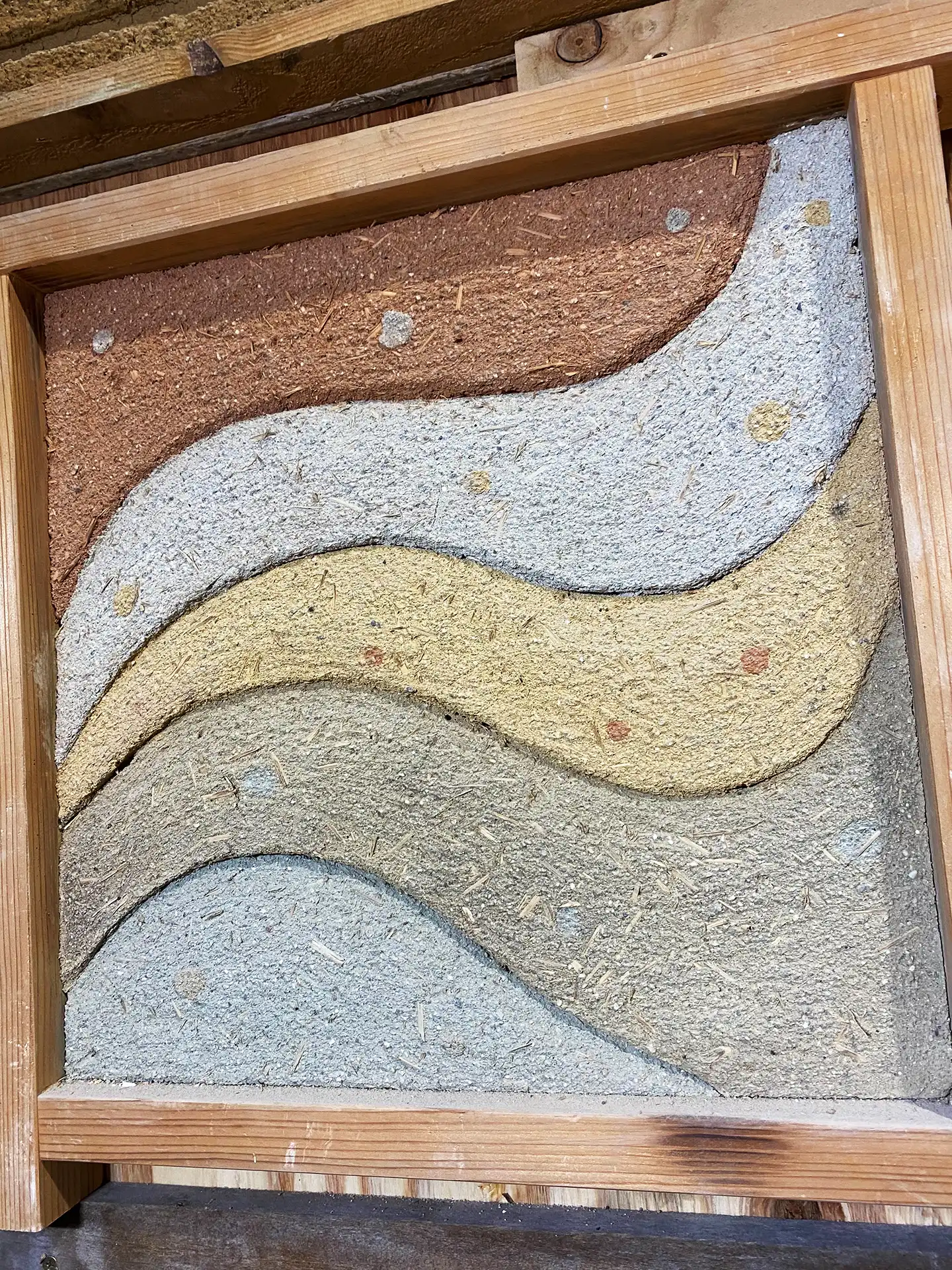 在木框內展示的塗り版築樣板，土層中清晰可見混入的稻草纖維與碎石顆粒，包含灰、黃、紅棕三色，展現豐富的材料層次。