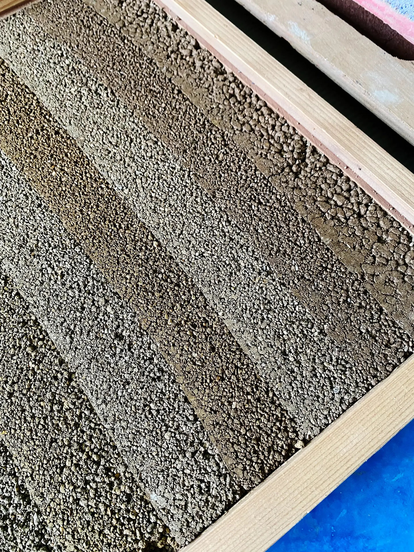 展示左官工藝中「塗り版築」的質感樣板，木框內由上而下排列不同顆粒大小與深淺土色的樣版，呈現粗獷且天然的孔隙感。