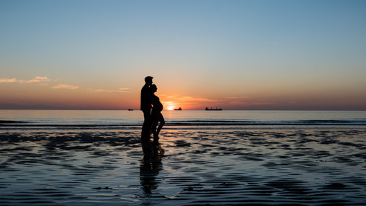 A silhouette of a pregnant woman standing with her partner with the sun rising behind them at Longsands Beach Tynemouth_maternity photography by Emma Solomon Photography