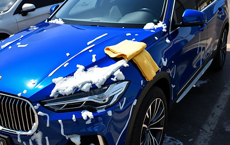 a visible blue shinny luxury SUV in a parking lot with a lot foam soap on it and a yellow