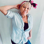 Woman with short blonde hair and a pink headband. Dressed in a blue denim shirt and jeans.