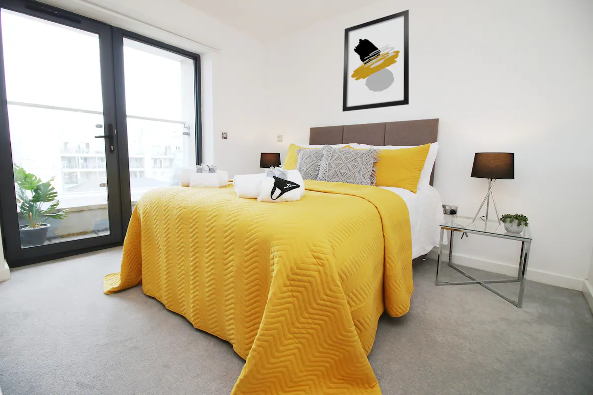 The bed is neatly made, with the yellow blankets complementing the soft tones of the bedding and decor
