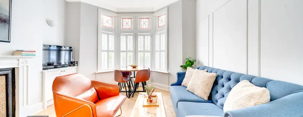 Interior shot of a Cardiff property living room featuring grey walls, a prominent orange couch, a contrasting blue couch, and a polished wood floor