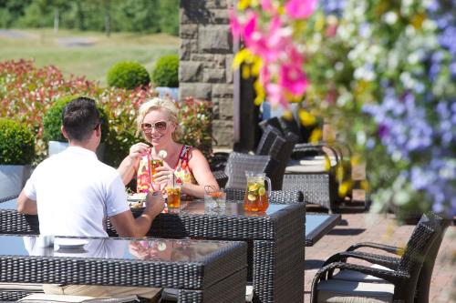 Two diners enjoy a meal al fresco at The Celtic Manor Resort in Newport, immersed in a picturesque outdoor setting, surrounded by lush greenery and under the warm glow of sunlight