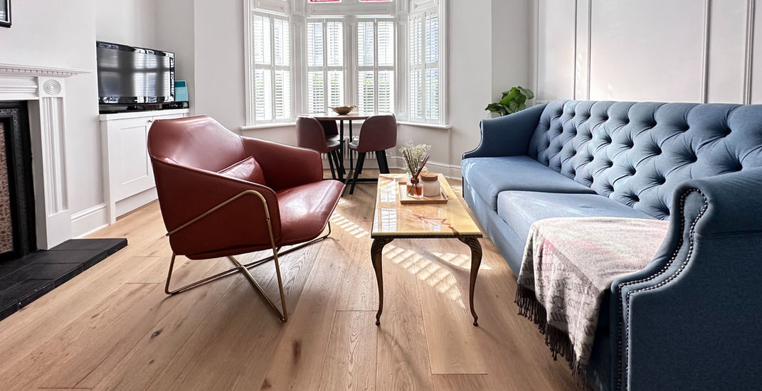 The living room of an AirFreedom dog-friendly property, featuring a blue couch and a red chair, creating a vibrant and inviting atmosphere. The space includes white walls and large windows with curtains, allowing natural light to fill the room.