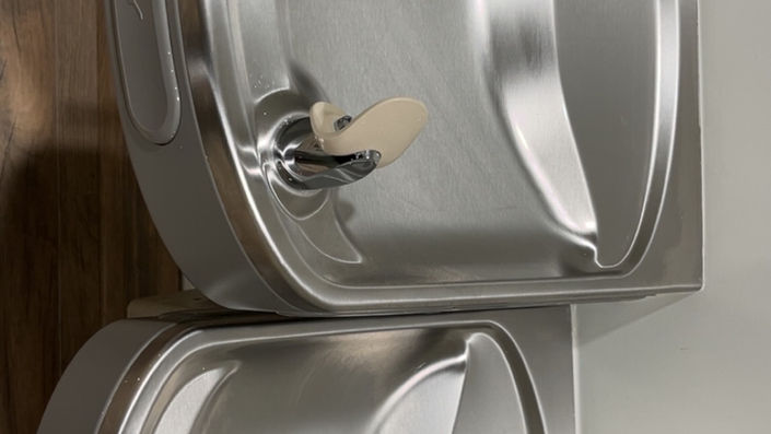 Two stainless steel urinals with handles, installed in a bathroom setting.