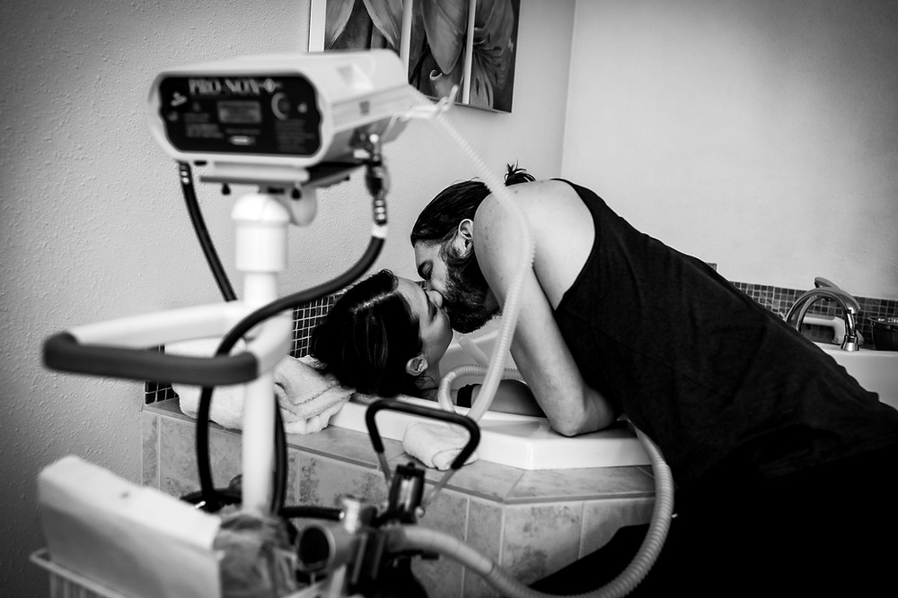 Home Birth in Durham, NC. Birthing person resting in the tub, kissing their partner.